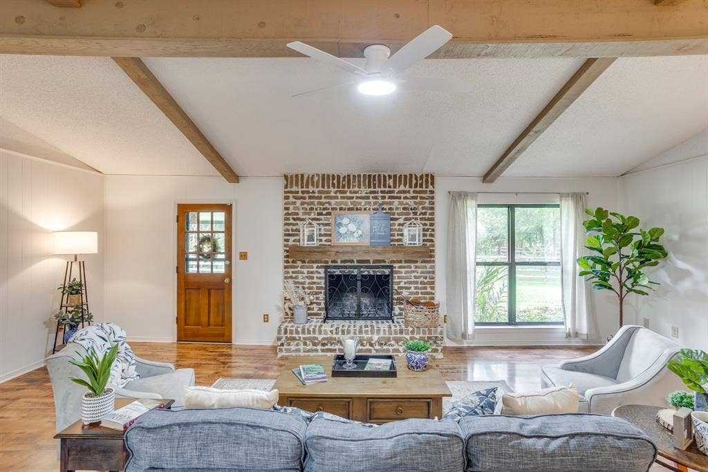 Exposed wood beams, wood-finish flooring, a brick fireplace with a wood mantel, a multi-pane window, and a wood-panel door with glass inserts