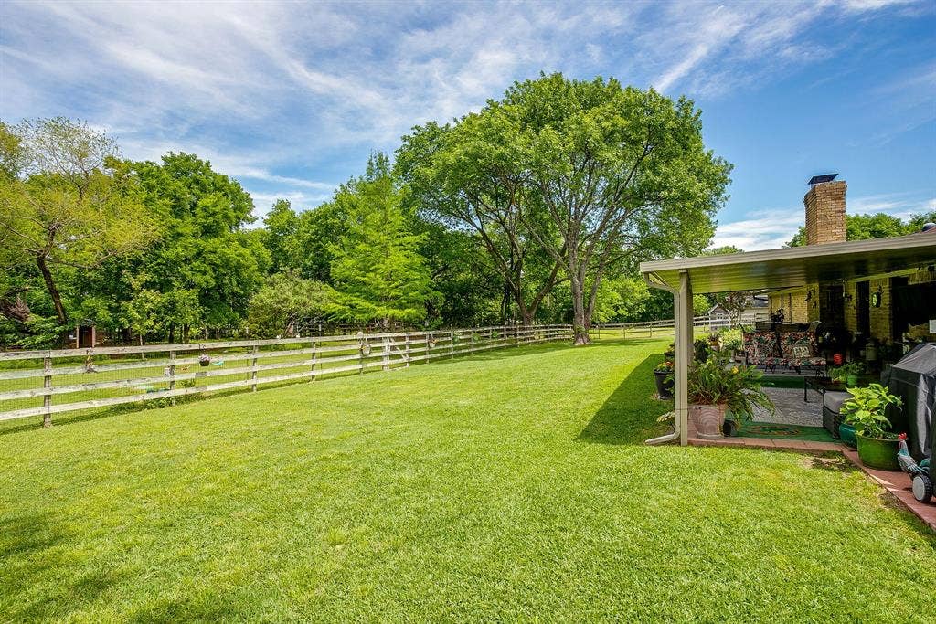Expansive lawn area, wood split-rail fencing, mature trees, covered patio, and a brick chimney