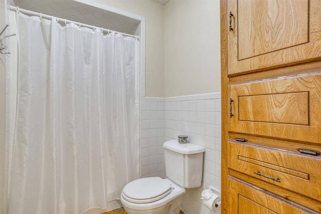 Built-in wood cabinetry with decorative pulls, white square tile wainscoting, and a white toilet