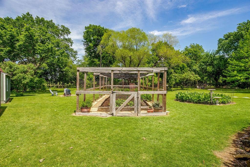 Expansive green lawn with mature trees, a built-in wooden garden enclosure, and a separate storage shed