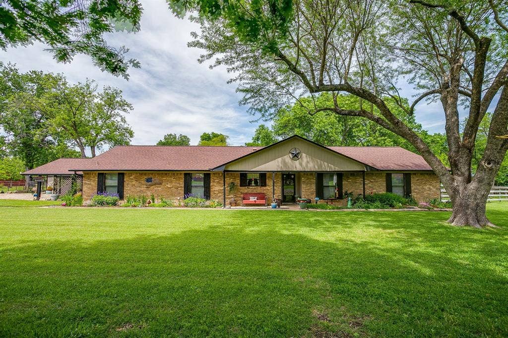Brick facade residence featuring a front lawn, mature trees, a covered entry, and dark window shutters