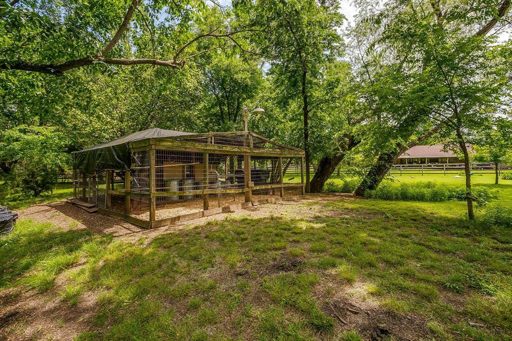 Wood-framed animal enclosure with a covered roof, surrounded by mature trees