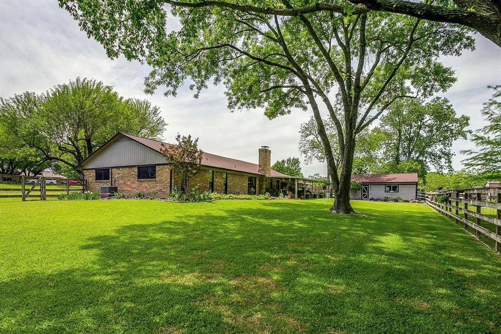 Expansive green lawn with mature trees, a wood fence, and a brick-clad structure