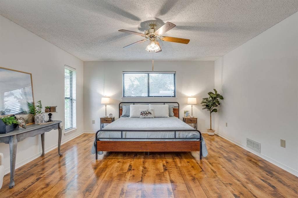 Wood-finish flooring, white walls, two windows with blinds, and a ceiling fan with light fixture
