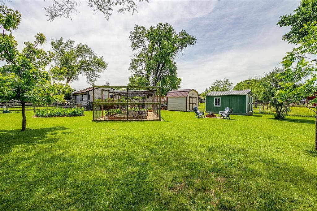 Expansive lawn with mature trees, two storage sheds, and a fenced garden area