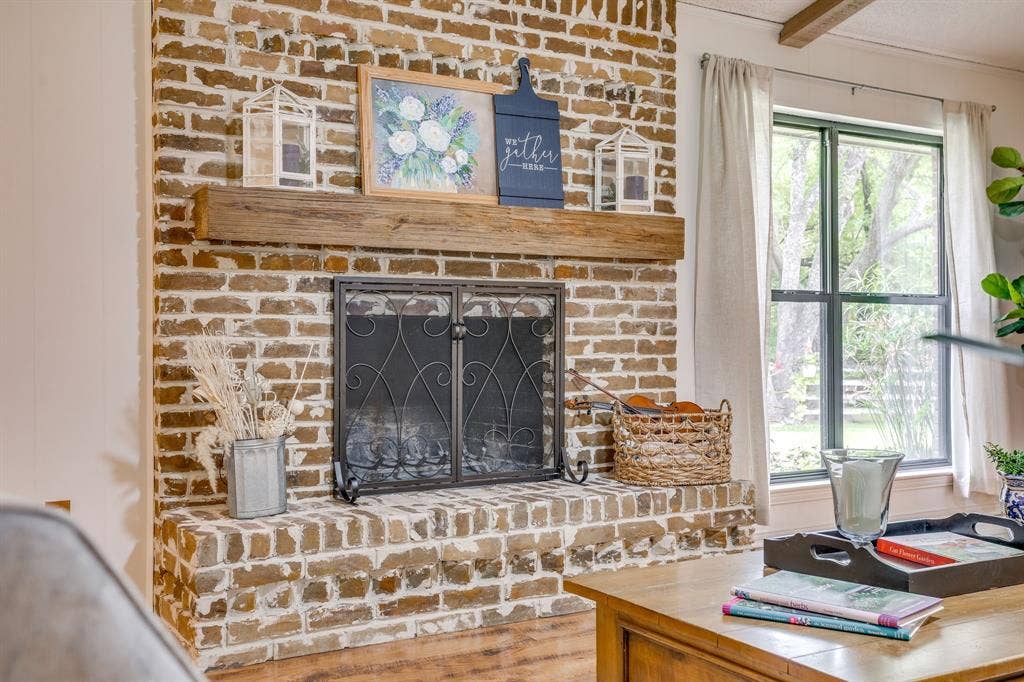 Brick fireplace with a substantial wood mantel, featuring a metal fire screen and a brick hearth