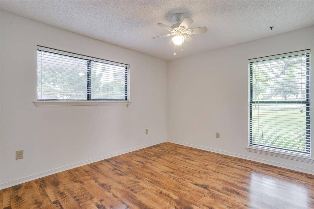 Wood-finish flooring with white baseboards, multiple windows with blinds, white walls, and a ceiling fan with integrated lighting