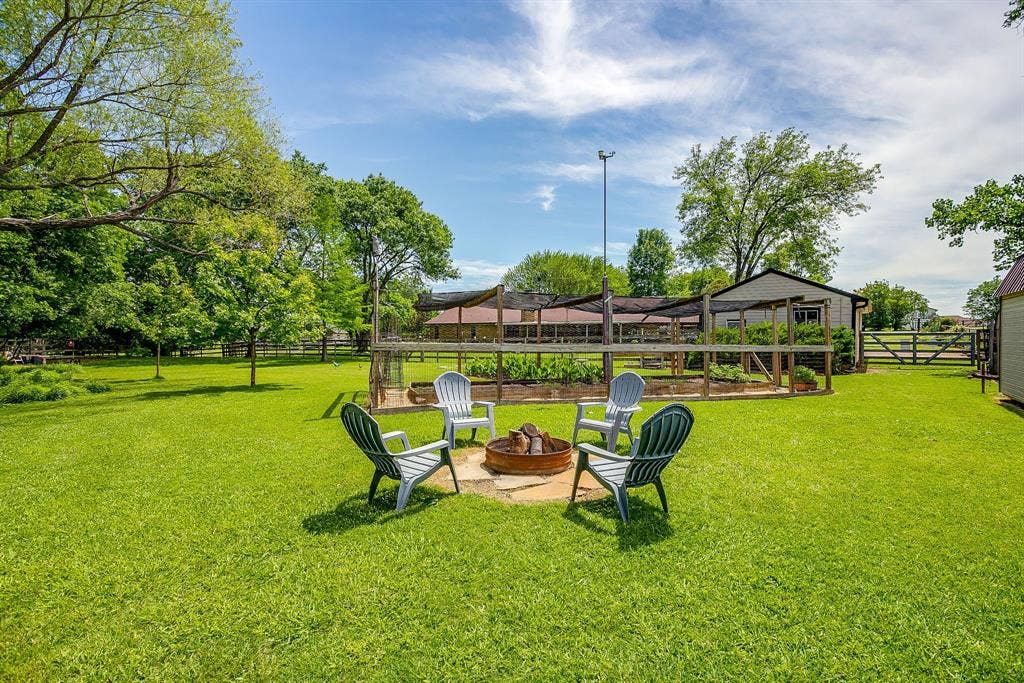 Expansive lawn with a built-in fire pit, surrounded by mature trees, and featuring a fenced garden bed