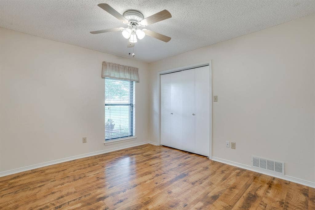 Wood-finish flooring, ceiling fan with integrated lighting, window with blinds, and built-in closet with bifold doors