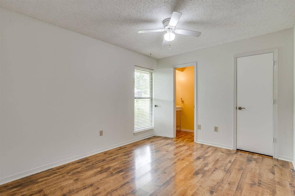Wood-finish flooring, white walls, ceiling fan with integrated lighting, window with blinds, and white interior doors