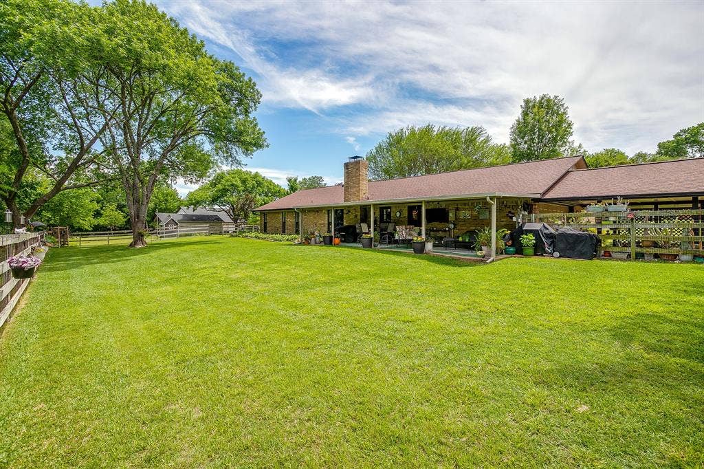 Expansive lawn area with mature trees, a covered patio, and brick exterior