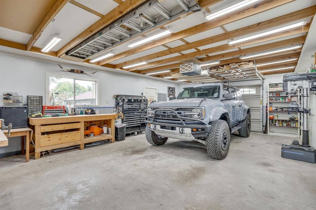 Garage space featuring exposed beam ceilings, multiple fluorescent light fixtures, a dedicated workbench area, and a window