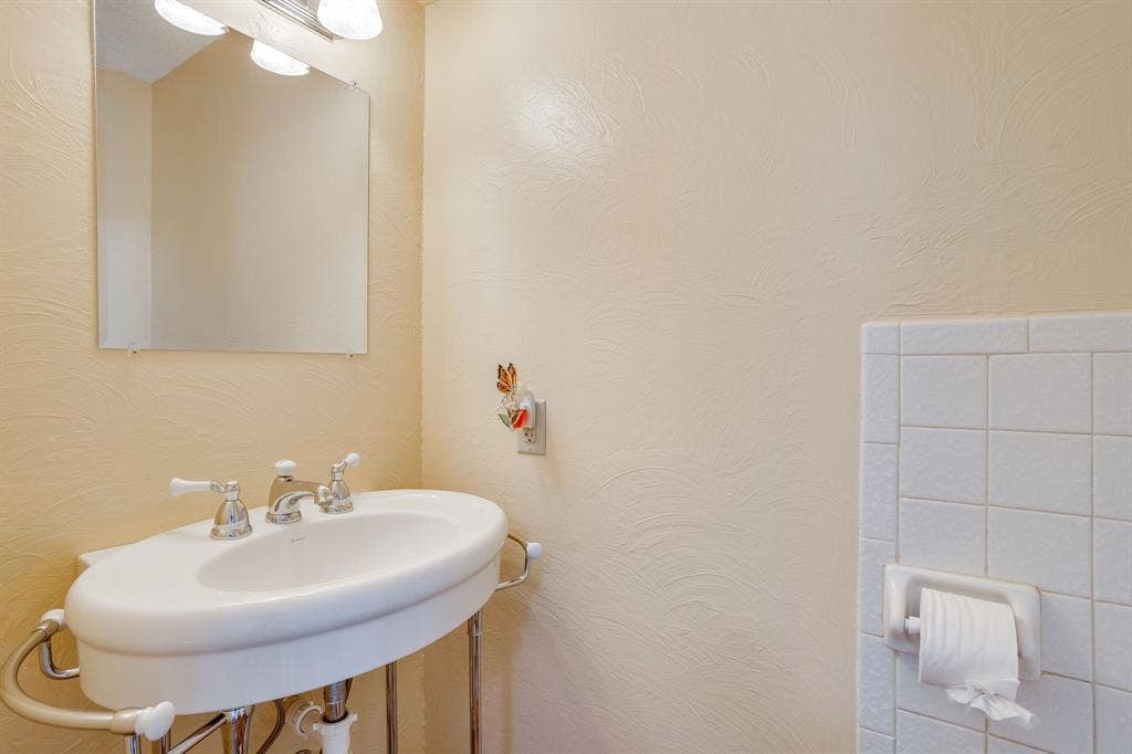 Wall-mounted sink with chrome fixtures, framed mirror, and tile wainscoting