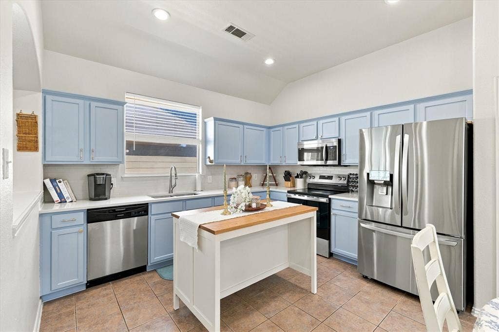 Kitchen featuring stainless steel appliances, light blue cabinetry, white countertops, and a center island with a wood-finish top