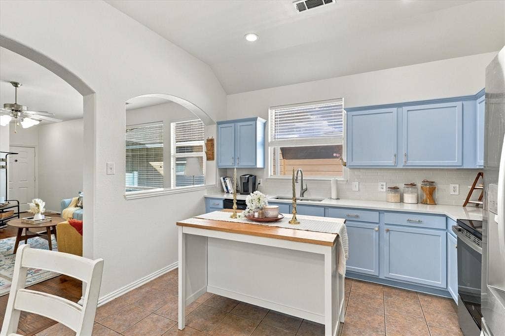 Kitchen featuring light blue cabinetry, white countertops, white subway tile backsplash, and a central island with a wood-finish top