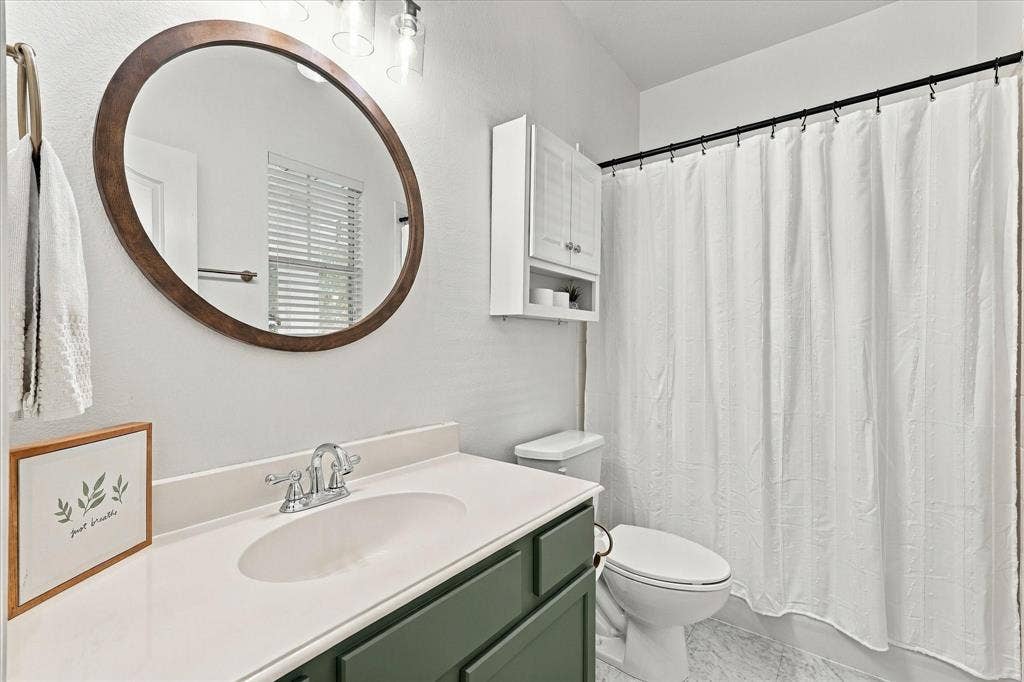 Bathroom featuring a vanity with a white countertop, oval wood-updated framed mirror, updated lighting and built-in wall cabinets!