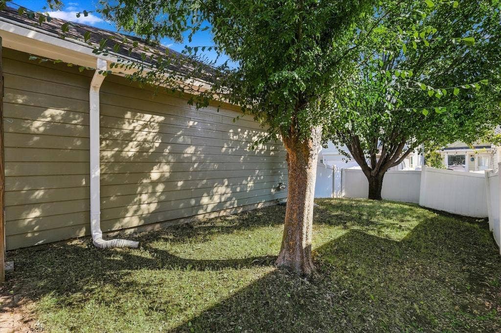 Green siding exterior with white gutters, multiple mature trees, and a white privacy fence