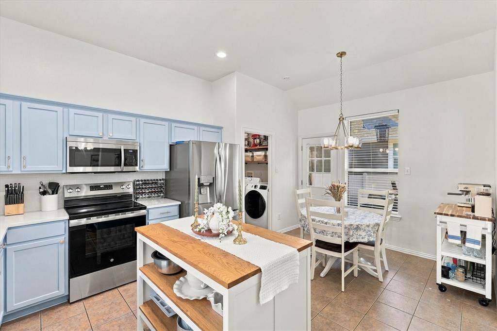 Kitchen featuring light blue cabinetry, stainless steel appliances, a center island with a wood countertop, and tile flooring