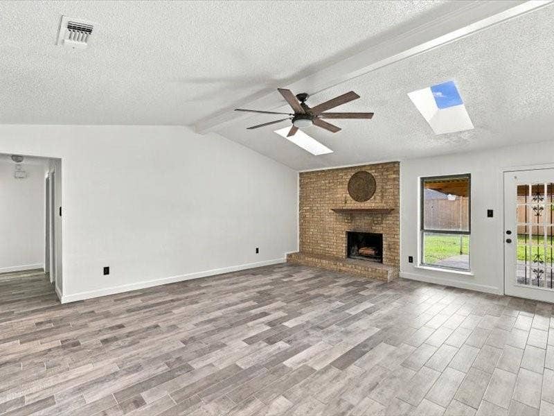 725 Southridge Court, Grand Prairie, TX 75052 Vaulted ceiling featuring skylights and a ceiling fan, brick fireplace with a wood mantel, wood-finish flooring, and a glass-paned exterior door