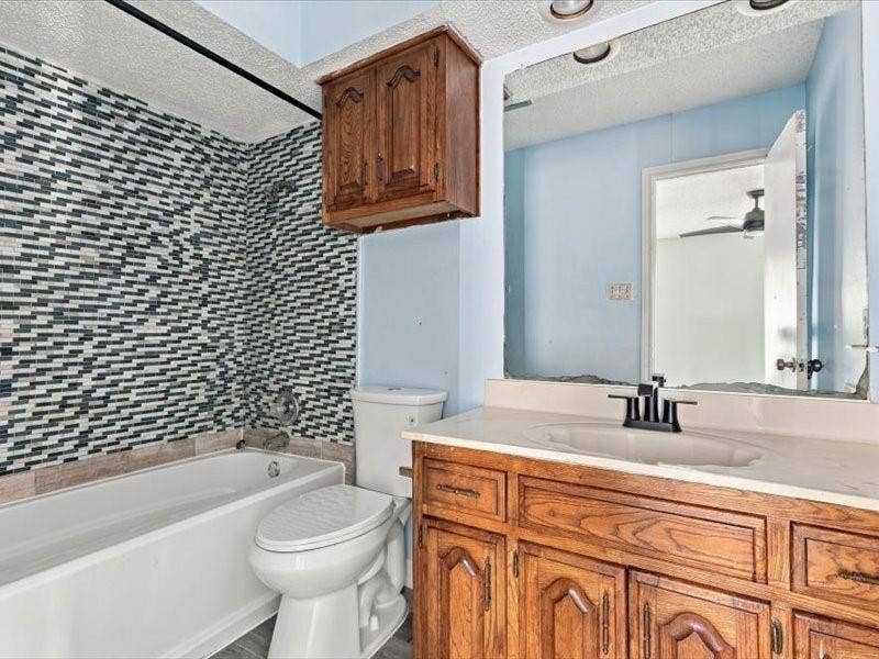 725 Southridge Court, Grand Prairie, TX 75052 Tub and shower combination with mosaic tile surround, wood-finish vanity with integrated sink, and wall-mounted wood-finish cabinet