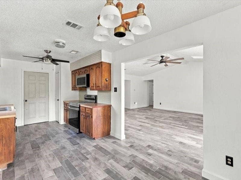 725 Southridge Court, Grand Prairie, TX 75052 Kitchen featuring wood cabinetry, stainless steel microwave, and wood-finish flooring extending into an adjacent living area with a ceiling fan