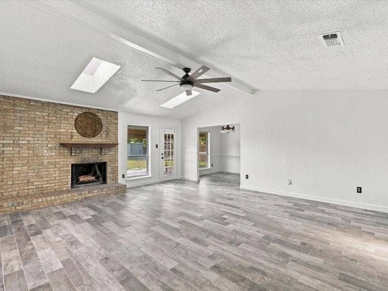 725 Southridge Court, Grand Prairie, TX 75052 Vaulted ceiling with skylights, wood-finish flooring, brick fireplace with wood mantle, and a glass-paneled door