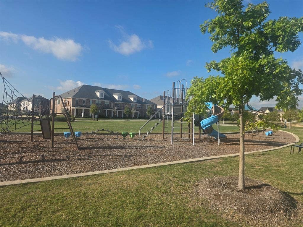 Community playground featuring climbing structures, slides, and mulch ground cover, situated on a manicured green space