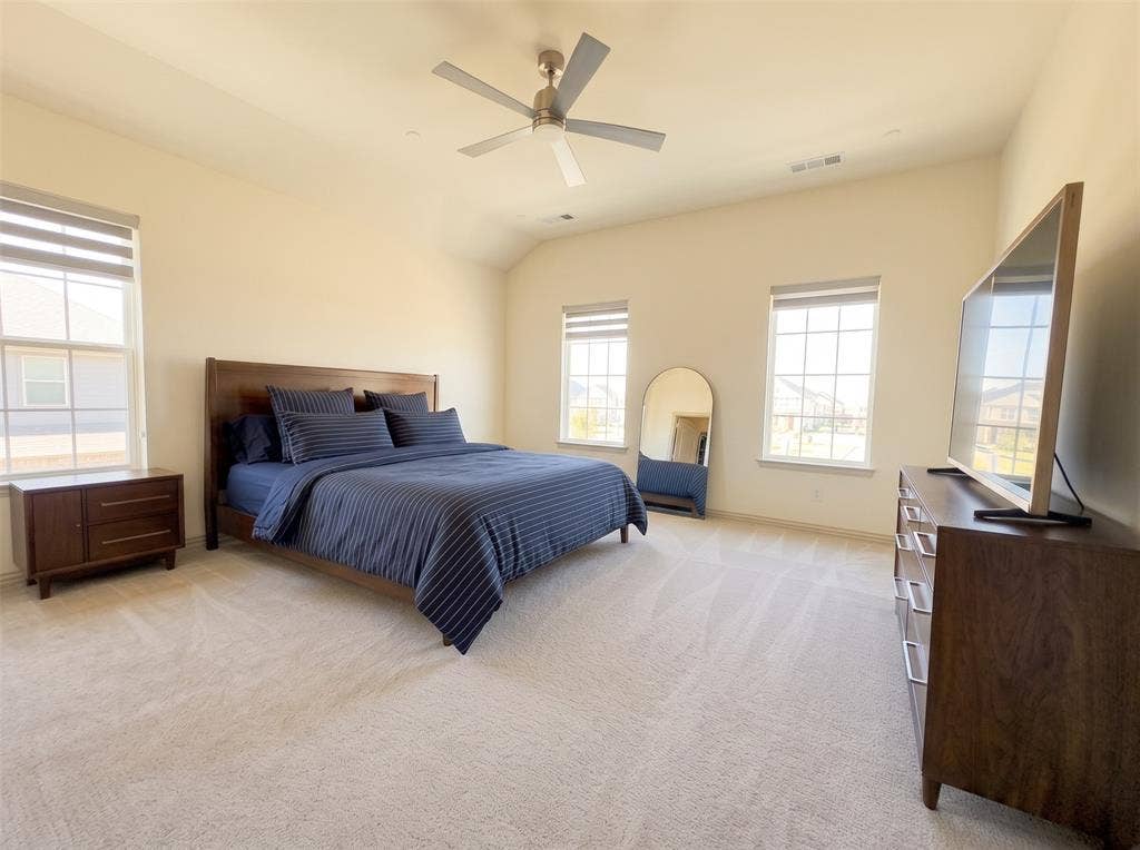 Vaulted ceilings featuring a brushed nickel ceiling fan, neutral wall-to-wall carpeting, and triple windows with integrated shades