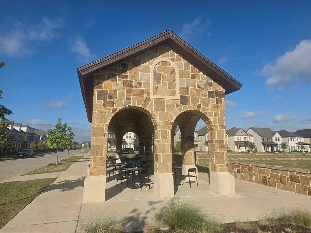 Outdoor pavilion featuring stone masonry, arched entryways, a gable roof, and concrete flooring