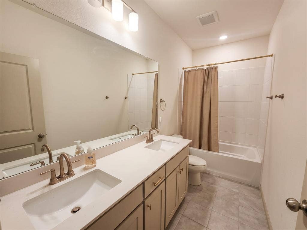 Dual-sink vanity with a solid-surface countertop, metallic-finish faucets, floor-to-ceiling mirror, and a tiled tub-and-shower combination