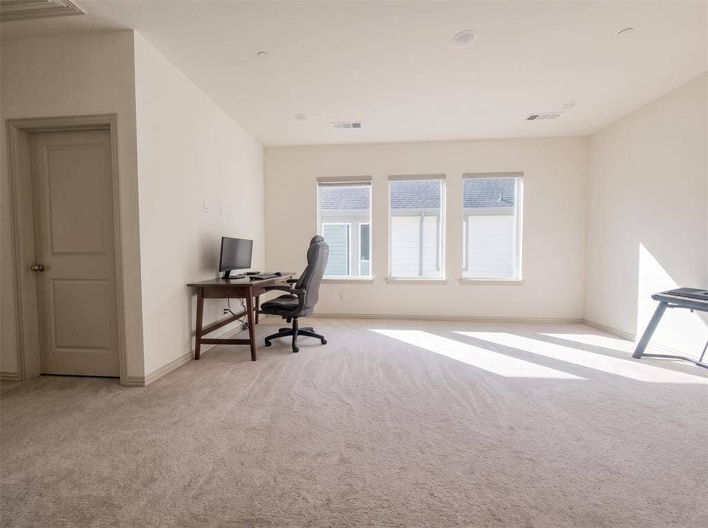 Neutral wall-to-wall carpeting, recessed ceiling lighting, and three large windows with light-filtering shades