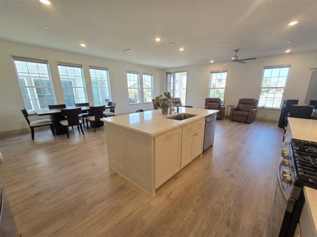 Open-concept kitchen featuring an expansive central island with a quartz countertop, wood-finish flooring, recessed lighting, and multiple windows