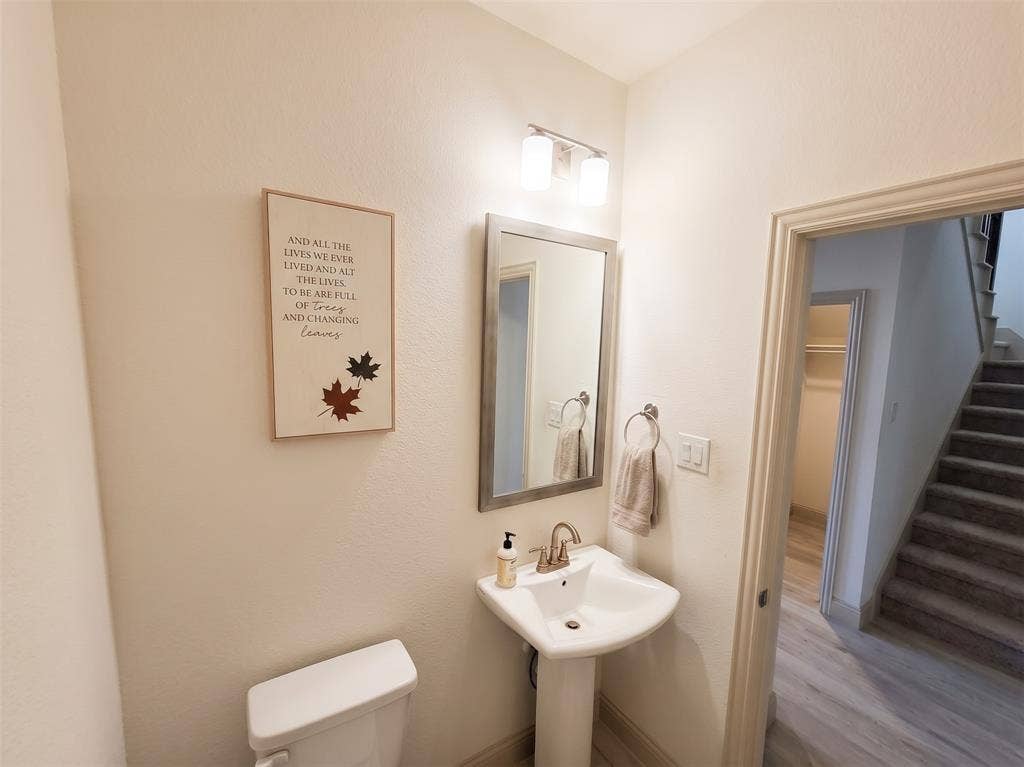 Powder room featuring a pedestal sink, wall-mounted two-light vanity fixture, and framed wall mirror