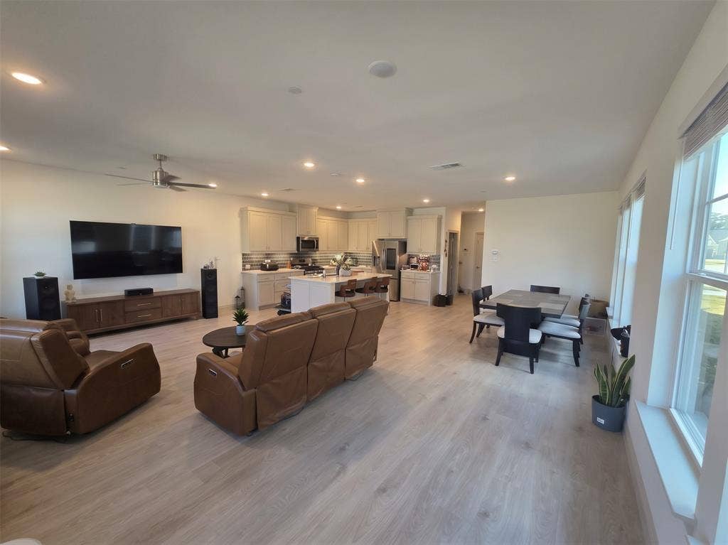 Open-concept area featuring wood-finish flooring, recessed lighting, a central kitchen island, and light-toned cabinetry