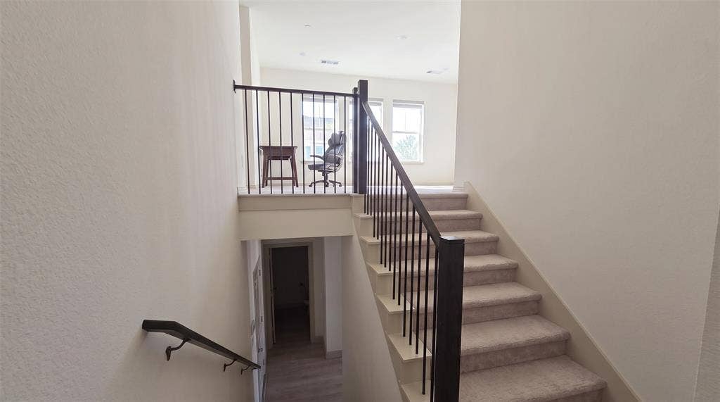 Staircase featuring carpeted steps, a dark metal balustrade, and a mounted metal handrail