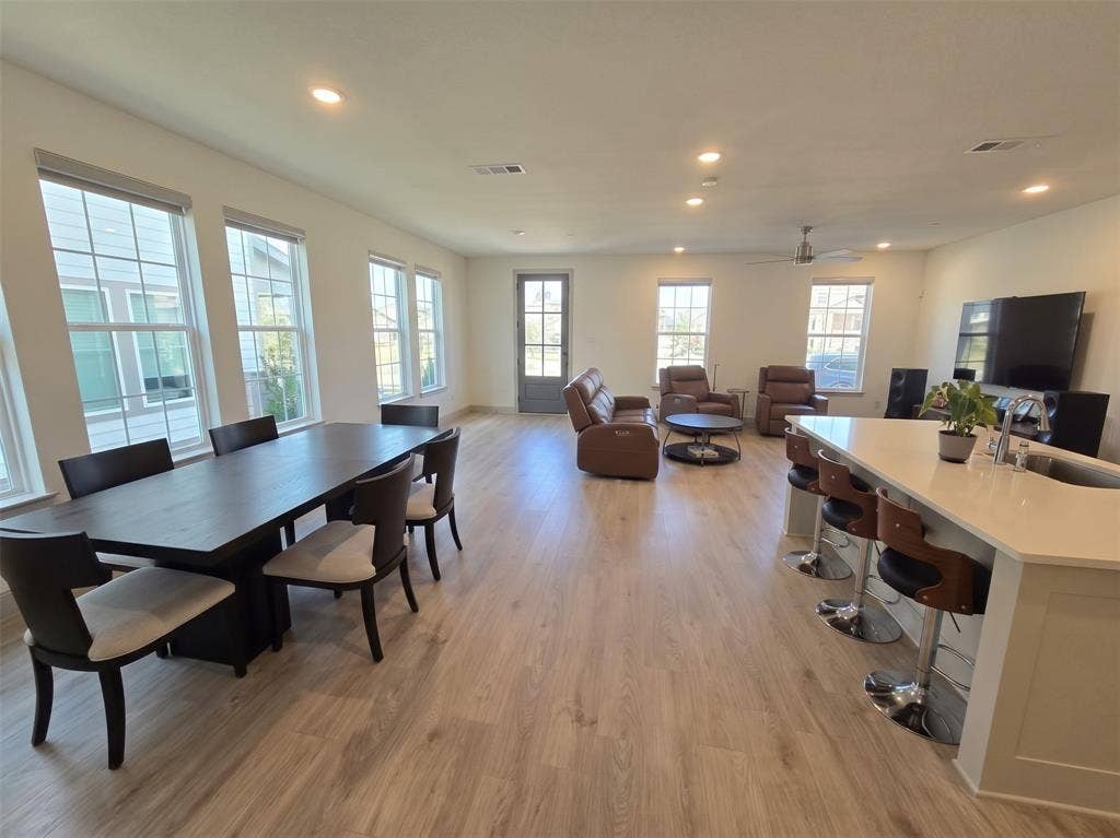 Open-concept room featuring light wood-finish flooring, recessed lighting, expansive windows with grid detailing, and a kitchen island with quartz countertops and an integrated undermount sink