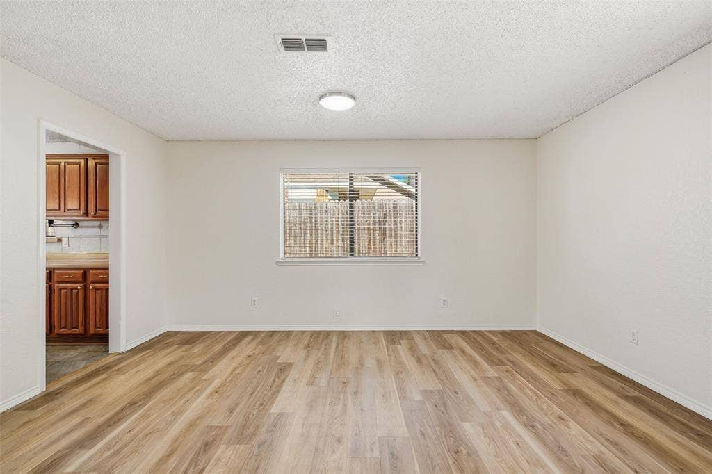 Wood-finish flooring, neutral wall tones, window with horizontal blinds, and a flush-mount ceiling light