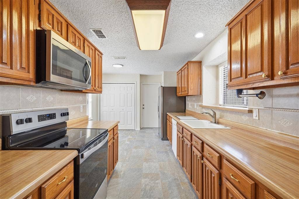 Galley kitchen featuring wood cabinetry, stainless steel appliances, wood-finish countertops, tiled backsplash, and recessed lighting
