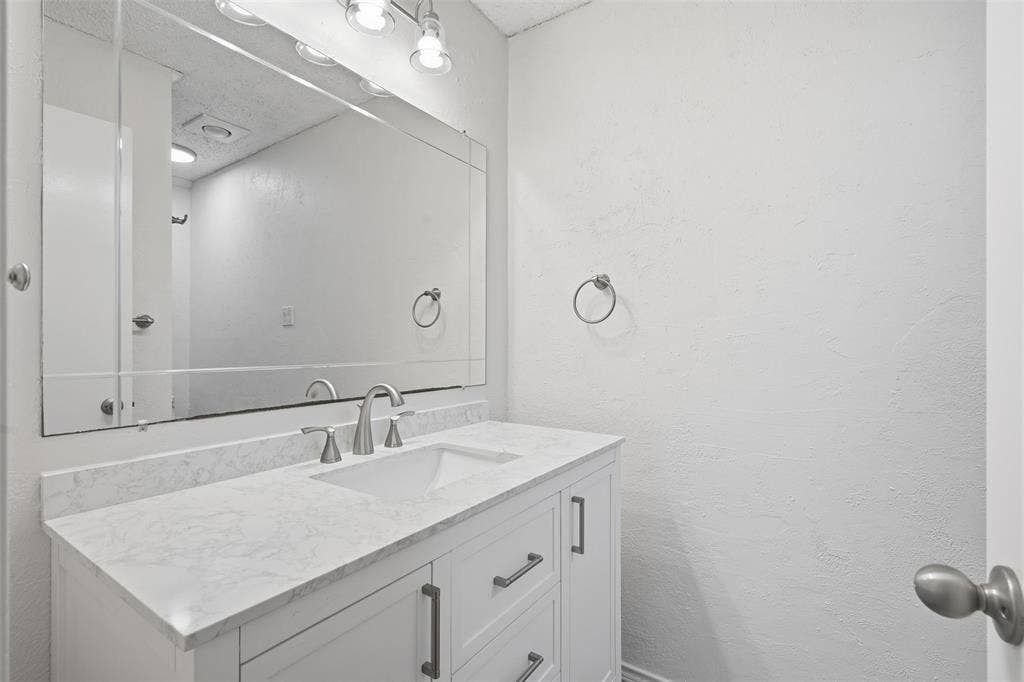 White vanity with a built-in sink, stone-finish countertop, and brushed nickel hardware