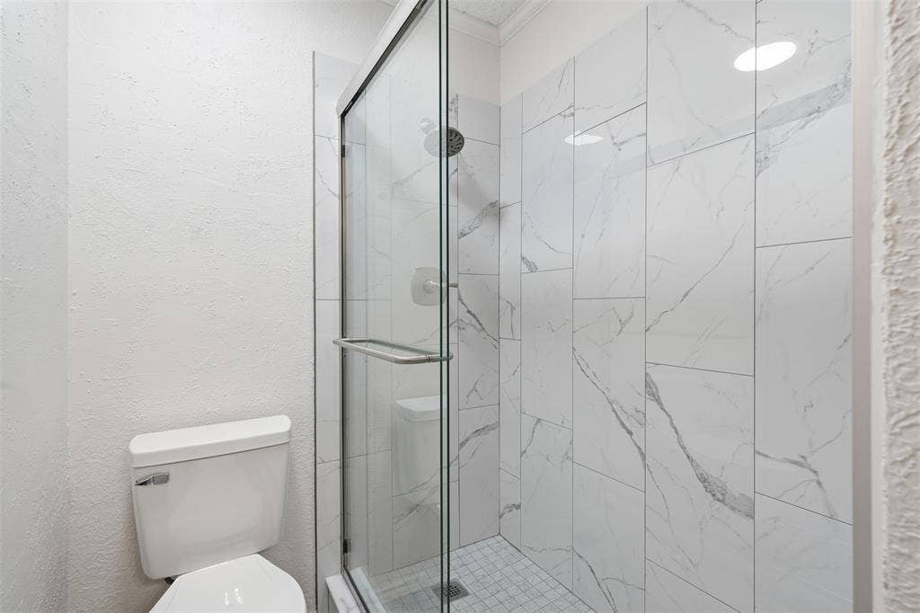 Frameless glass shower enclosure with a chrome handle, white subway tile shower walls with grey veining, and a tiled shower floor