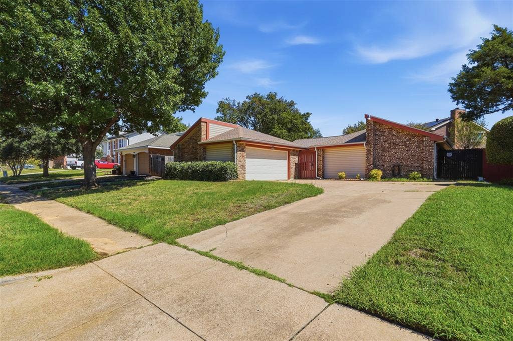 Brick exterior with a peaked roofline, mature trees, and a concrete driveway