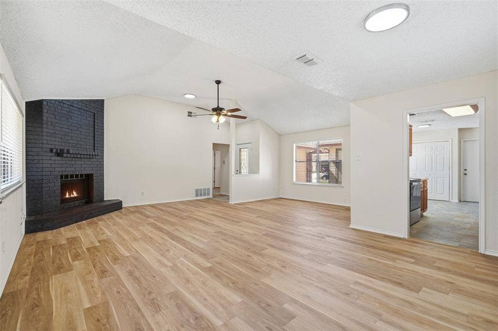 Spacious living area featuring a black brick fireplace, wood-finish flooring, vaulted ceiling, and recessed lighting