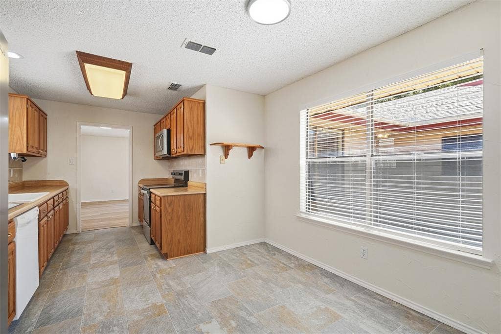 Kitchen featuring wood-finish cabinetry, built-in microwave, tile-finish flooring, and a large window with blinds