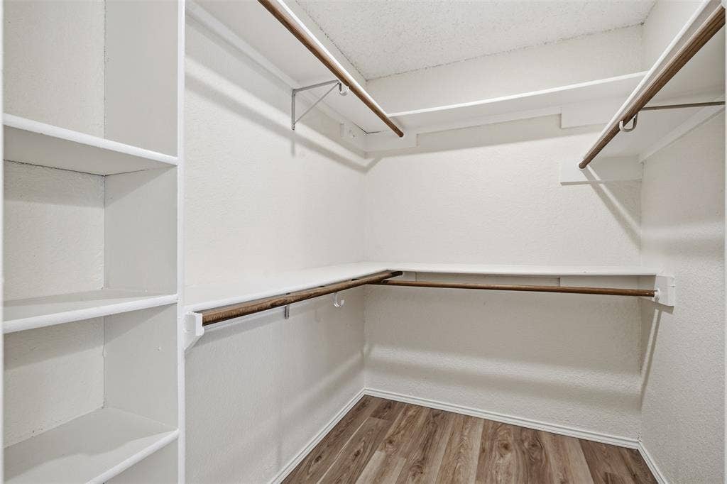 Walk-in closet featuring built-in shelving, multiple hanging rods, and wood-finish flooring