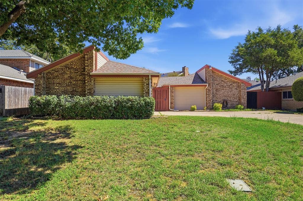Brick facade featuring a multi-tone shingle roof, attached garage, and a manicured hedge