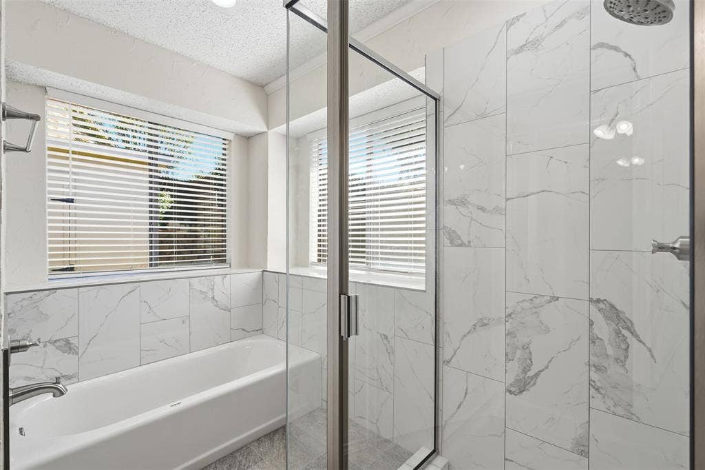 Glass-enclosed shower with a rainfall showerhead, white subway tile surround, integrated bathtub, and dual windows with blinds