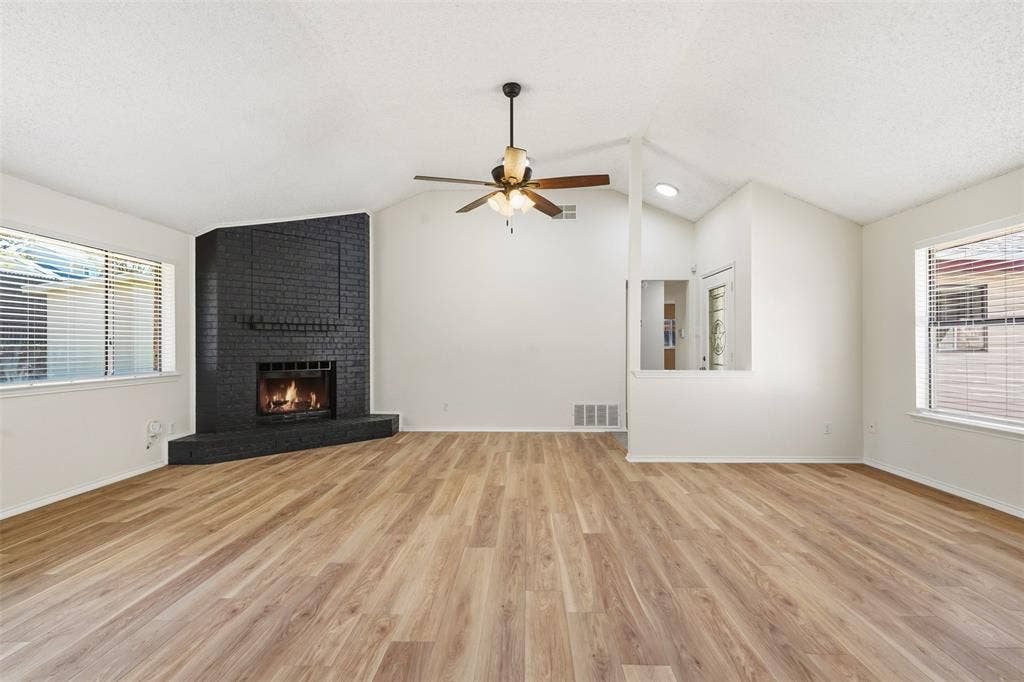 Vaulted ceiling, wood-finish flooring, corner brick fireplace, ceiling fan, and multiple windows