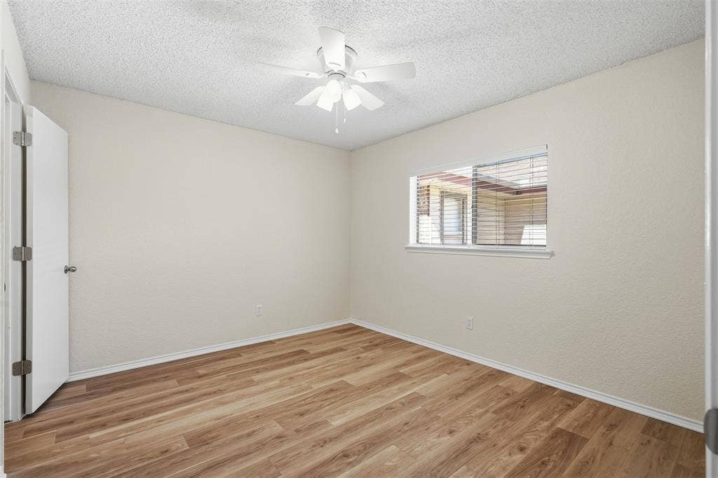 Room featuring wood-finish flooring, a ceiling fan, and a window with blinds
