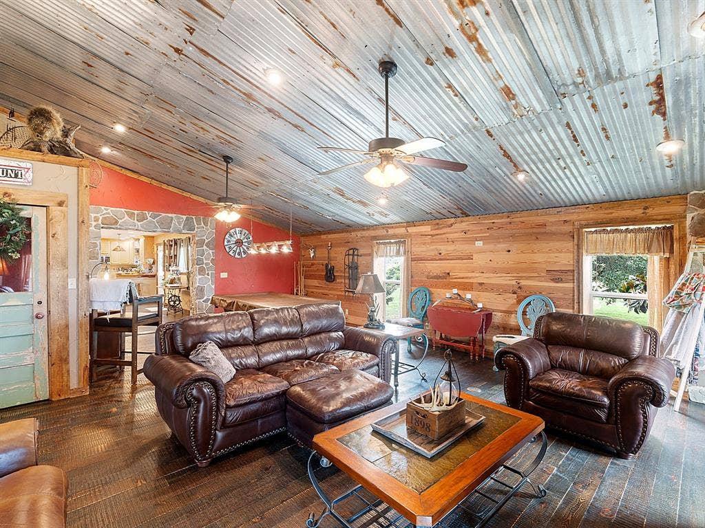 5801 County Road 4128, Scurry, TX 75158 Vaulted ceiling with corrugated metal cladding, horizontal wood-plank wall paneling, natural stone accents, dark wood-finish flooring, and integrated ceiling fans