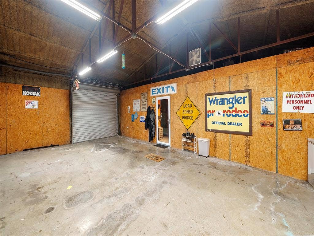 5801 County Road 4128, Scurry, TX 75158 Spacious utility garage featuring exposed steel truss ceiling, concrete flooring, roll-up overhead door, and oriented strand board wall paneling